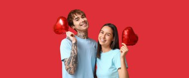 Kırmızı arka planda kalp şeklinde balonları olan mutlu genç çift.