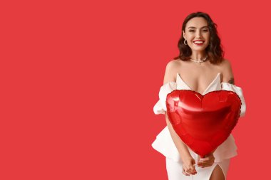 Kırmızı arka planda kalp şeklinde hava balonu olan güzel genç bir kadın.
