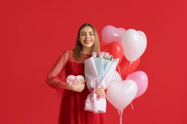 Hediye kutusu, çiçek buketi ve kırmızı arka planda kalp şeklinde balonları olan güzel bir kadın. Sevgililer Günü kutlaması