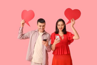 Cep telefonları ve pembe arka planda konuşma baloncukları olan genç bir çift. Online randevu