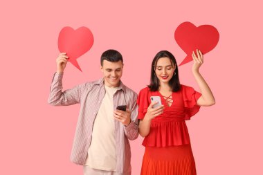 Young couple with mobile phones and speech bubbles on pink background. Online dating clipart