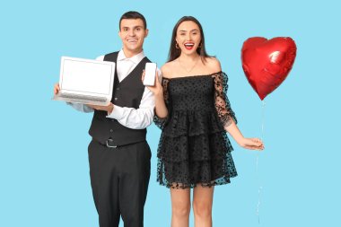 Cep telefonu, dizüstü bilgisayar ve mavi arka planda kalp şeklinde hava balonu olan genç bir çift. Online randevu