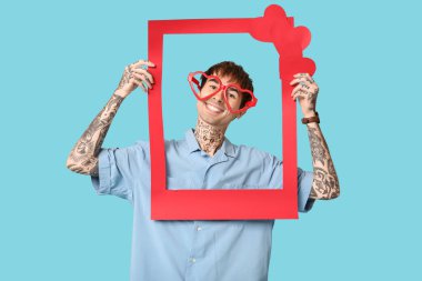 Kalp şeklinde gözlüklü komik genç adam ve mavi arka planda kırmızı çerçeve. Sevgililer Günü kutlaması