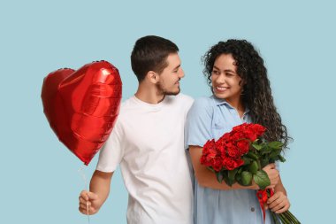 Mavi arka planda Sevgililer Günü için kalp şeklinde balonları ve gül çiçekleri olan genç bir çift.