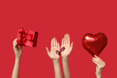 Hediye kutusu olan kadın eller, kırmızı arka planda kalp ve kalp şeklinde balon. Sevgililer Günü kutlaması