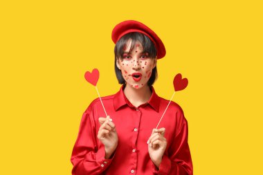 Sevgililer Günü için yaratıcı makyajı ve sarı arka planda kalpleri olan genç ve güzel bir kadın.