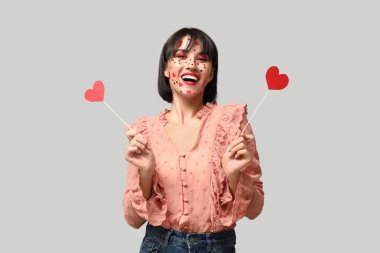 Beautiful young young woman with creative makeup for Valentines Day and hearts on grey background