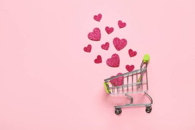 Pembe arka planda kağıt kalpli küçük bir alışveriş arabası. Sevgililer Günü kutlaması