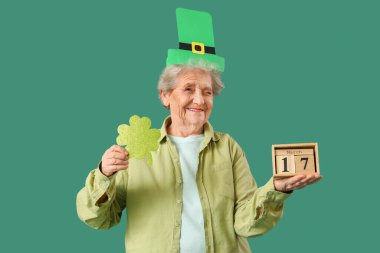 Kağıt yonca ve takvimle yeşil arka planda yanıp sönen St. Patrick Günü kutlamaları için cüce şapkalı mutlu son sınıf kadını.