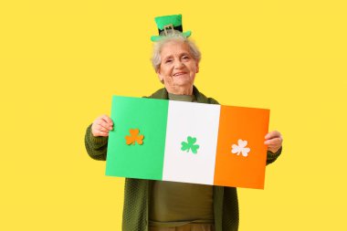 Sarı arka planda İrlanda bayrağı ve cüce şapkalı mutlu yaşlı kadın. Aziz Patrick Günü kutlaması