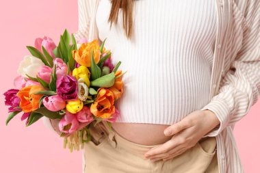 Pembe arka planda bir buket lalesi olan hamile bir kadın. Uluslararası Kadınlar Günü