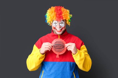 Young man as clown with crazy smile and whoopee cushion on black background clipart