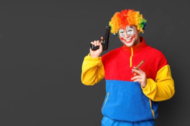 Siyah arka planda purosu ve silahı olan deli bir palyaço gibi gülümsüyor.