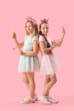 Cute little girls in princess costumes with graggers on pink background. Purim celebration clipart