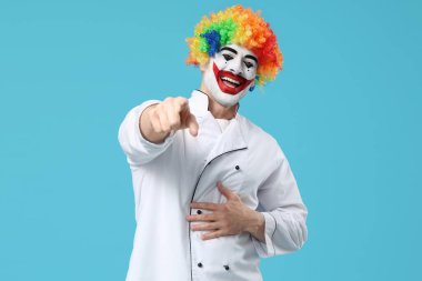 Palyaço aşçısı olarak gülen genç adam mavi arka plandaki birini işaret ediyor.