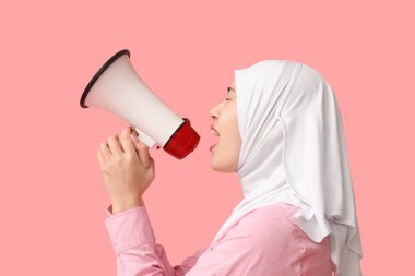 Genç Asyalı Müslüman kadın pembe arka planda megafona bağırıyor. Ulusal Duyulma Günü