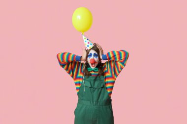 Üzgün palyaço gibi giyinmiş, pembe arka planda balonu olan genç bir kadın. 1 Nisan şakası