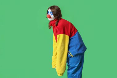 Yeşil arka planda üzgün bir palyaço gibi giyinmiş genç bir kadın. 1 Nisan şakası