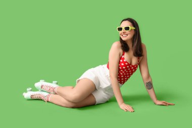 Yeşil arka planda oturan patenli güzel genç bir kadın.