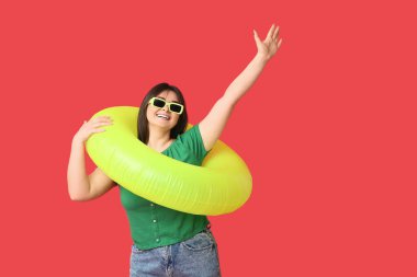 Kırmızı arka planda şişme yüzüğü olan mutlu genç bir kadın.