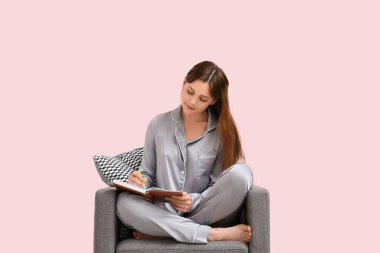 Pijamalı genç bir kadın evdeki siyah koltuğa not defterine yazıyor. Uzak çalışma konsepti