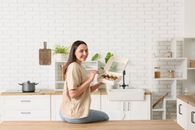 Mutfakta çikolata kaplı çilek dolu bir kutu tutan güzel bir kadın.