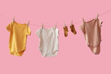 Farklı bebek kıyafetleri ve pembe arka planda asılı çoraplar.