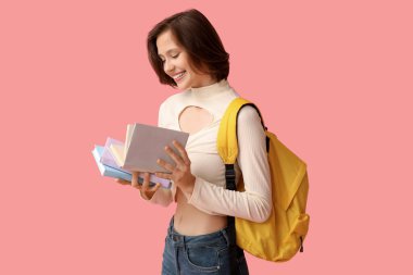 Sırt çantası ve pembe arka plan kitapları olan güzel bir kız öğrenci.
