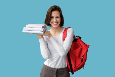 Mavi arka planda kitapları ve sırt çantası olan güzel bir kız öğrenci.