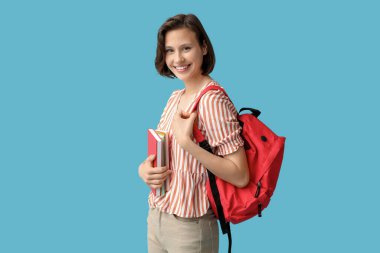 Sırt çantası ve mavi arka planda defterleri olan mutlu kız öğrenci.