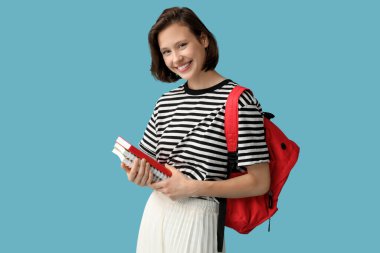 Sırt çantası ve mavi arka planda defterleri olan mutlu kız öğrenci.