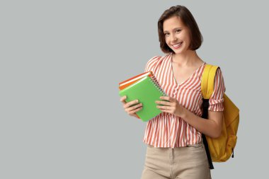 Gri arka planda not defterleri ve sırt çantasıyla güzel bir kız öğrenci.