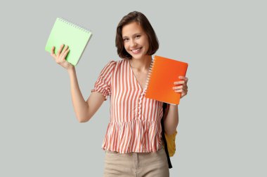 Gri arka plan üzerine not defterleri olan güzel bir kız öğrenci.