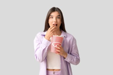 Beyaz arka planda patlamış mısır yiyen genç bir kadın.