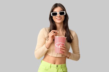 3 boyutlu sinema gözlüklü güzel bir kadın gri arka planda patlamış mısır yiyor.