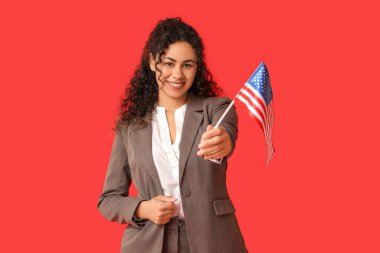 Kırmızı arka planda Amerikan bayrağı olan güzel, mutlu, Afro-Amerikalı bir iş kadını.