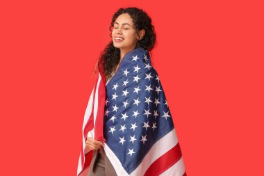 Kırmızı arka planda Amerikan bayrağı olan güzel, mutlu, Afro-Amerikalı bir iş kadını.