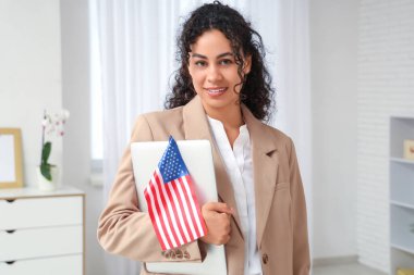 Güzel, mutlu, Afro-Amerikan iş kadını, ABD bayrağı ve laptopuyla ofiste.