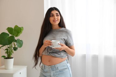 Genç hamile kadın yatak odasında çay içiyor.