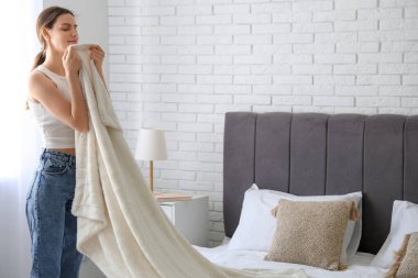 Genç bir kadın yumuşak battaniyeyle evde yatak yapıyor.