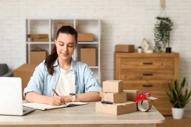 Depoda çalışan, elinde defter ve paket kutusu olan genç bir kadın.