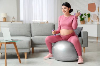 Güzel hamile kadın oturma odasında spor yapıyor.