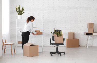 İş kadını taşınma gününde ofisteki raflardan karton kutuları alıyor.