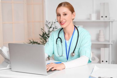 Klinikte çalışan dizüstü bilgisayarı ve steteskopu olan mutlu kadın doktor.