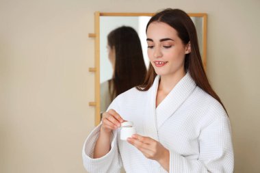 Banyodaki duştan sonra elinde krema kavanozuyla genç bir kadın.