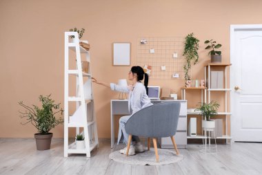 Genç bir kadın evdeki raftan kitap alıyor.