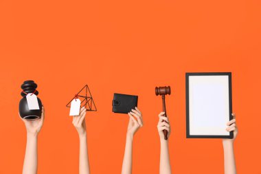 Turuncu arka planda açık arttırma tokmağı, cüzdanı ve antika eşyaları olan kadın eller.