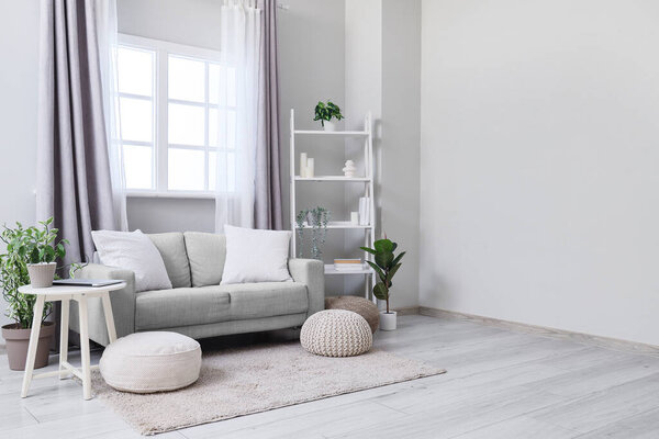 Cozy sofa, coffee table, shelving unit, houseplants and poufs in interior of living room