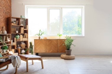 Koltuk, çekmece sandığı, kitap ve çiçeklerle dolu raf üniteleri ev kütüphanesinin içinde.