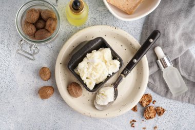 Hafif arka planda Shea yağı, fındık ve gerekli yağ şişeleri ile tabak